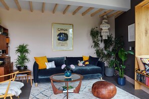 Ein Wohnzimmer mit einem dunkelblauen Sofa, einem Couchtisch, einem Ledersitzhocker und einer hängenden Deckenleuchte.
