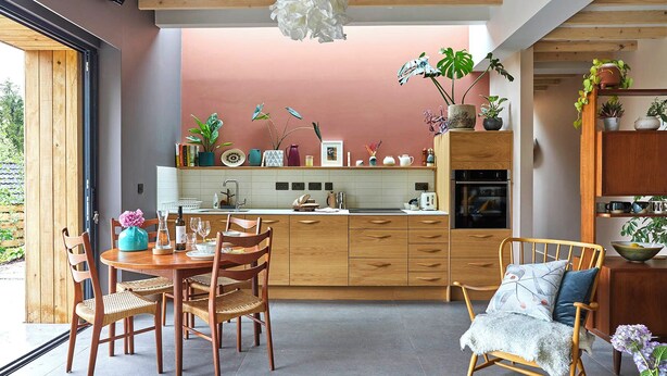 A modern kitchen with wooden cabinets, a dining area with wicker chairs, and a view through a large window. - Award-winning Nuthatch Retreat | Cinema | Landscaped gardens | Bathe under stars (Blakeney)