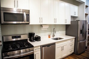 A modern kitchen with stainless steel appliances, white cabinetry, and a tiled backsplash.