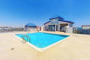 A swimming pool with a blue roof structure, a fenced area, and a clear sky. - Sunset Pointe 302 - Pool, Prime Location (Ocean City)