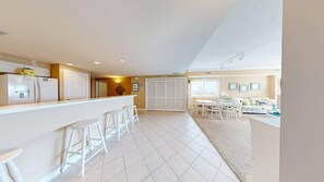 A modern kitchen with white appliances, a bar area with stools, and a dining area with a table and chairs. - Sunset Pointe 302 - Pool, Prime Location (Ocean City)