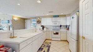 A modern kitchen with white cabinetry, a microwave, an oven, and a refrigerator. There is a rug with nautical designs on the floor. - Sunset Pointe 302 - Pool, Prime Location (Ocean City)