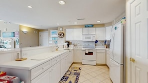 A modern kitchen with white cabinetry, a microwave, an oven, and a refrigerator. There is a rug with nautical designs on the floor. - Sunset Pointe 302 - Pool, Prime Location (Ocean City)