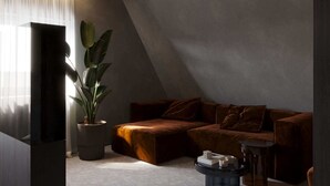 Un soggiorno moderno con soffitto spiovente, un divano dai toni scuri, una pianta in vaso e un piccolo tavolino rotondo.