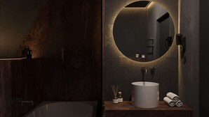 Un bagno moderno con una vasca da bagno freestanding, uno specchio rotondo illuminato e un lavandino bianco con un asciugamano.