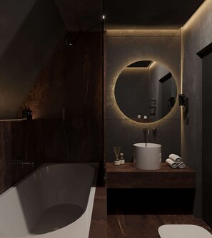Ein modernes Badezimmer mit einer freistehenden Badewanne, einem runden Spiegel mit Beleuchtung und einem weißen Waschbecken mit Handtuch.