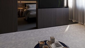 Una camera d'albergo moderna con un letto, una televisione a schermo piatto, un comodino con una lampada e vista sulla città attraverso tende trasparenti.