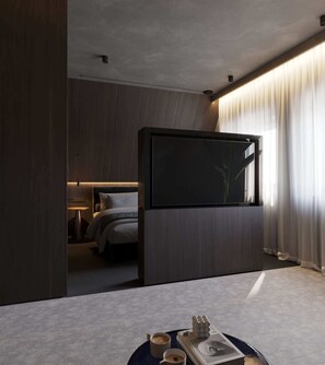 Ein modernes Hotelzimmer mit einem Bett, einem Flachbildfernseher, einem Nachttisch mit Lampe und Blick auf die Stadt durch leichte Vorhänge.