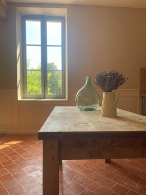 Ein Zimmer mit einem Holztisch, einem grünen Strauß in einer Vase und einem weißen Krug mit Blumen.