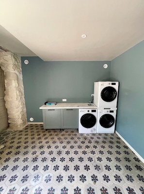 A laundry room with two stacked washing machines, a stone wall, and a tiled floor. - 90m2 air-conditioned vacation rental / Pool & Garden / Near the beaches (Fleury)