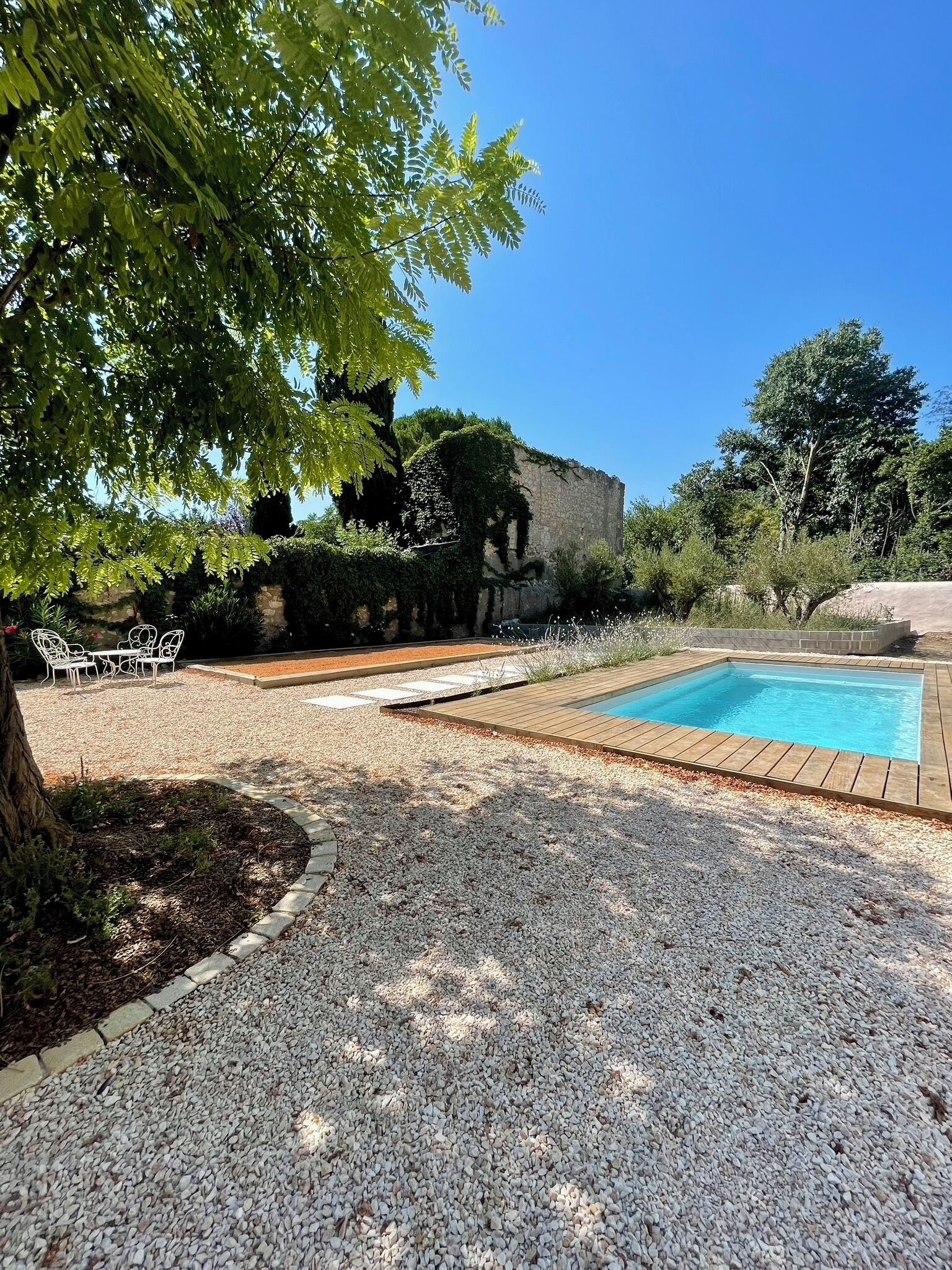 Une piscine entourée de gravier, avec un mur de pierre et de la verdure en arrière-plan.