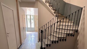 A hallway with patterned floor tiles, a staircase with a metal railing, and a door leading to an outdoor area. - 90-square-meter air-conditioned vacation rental / Pool & Garden / Near the beaches (Fleury)