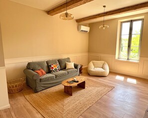 Ein Wohnzimmer mit einer Couch, einem Couchtisch, einem Sessel und einem großen Fenster mit Blick auf Grünflächen.