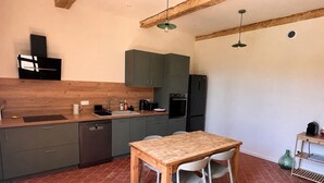 A compact kitchen with a wooden table and chairs, a dishwasher, and a refrigerator. - 90-square-meter air-conditioned vacation rental / Pool & Garden / Near the beaches (Fleury)