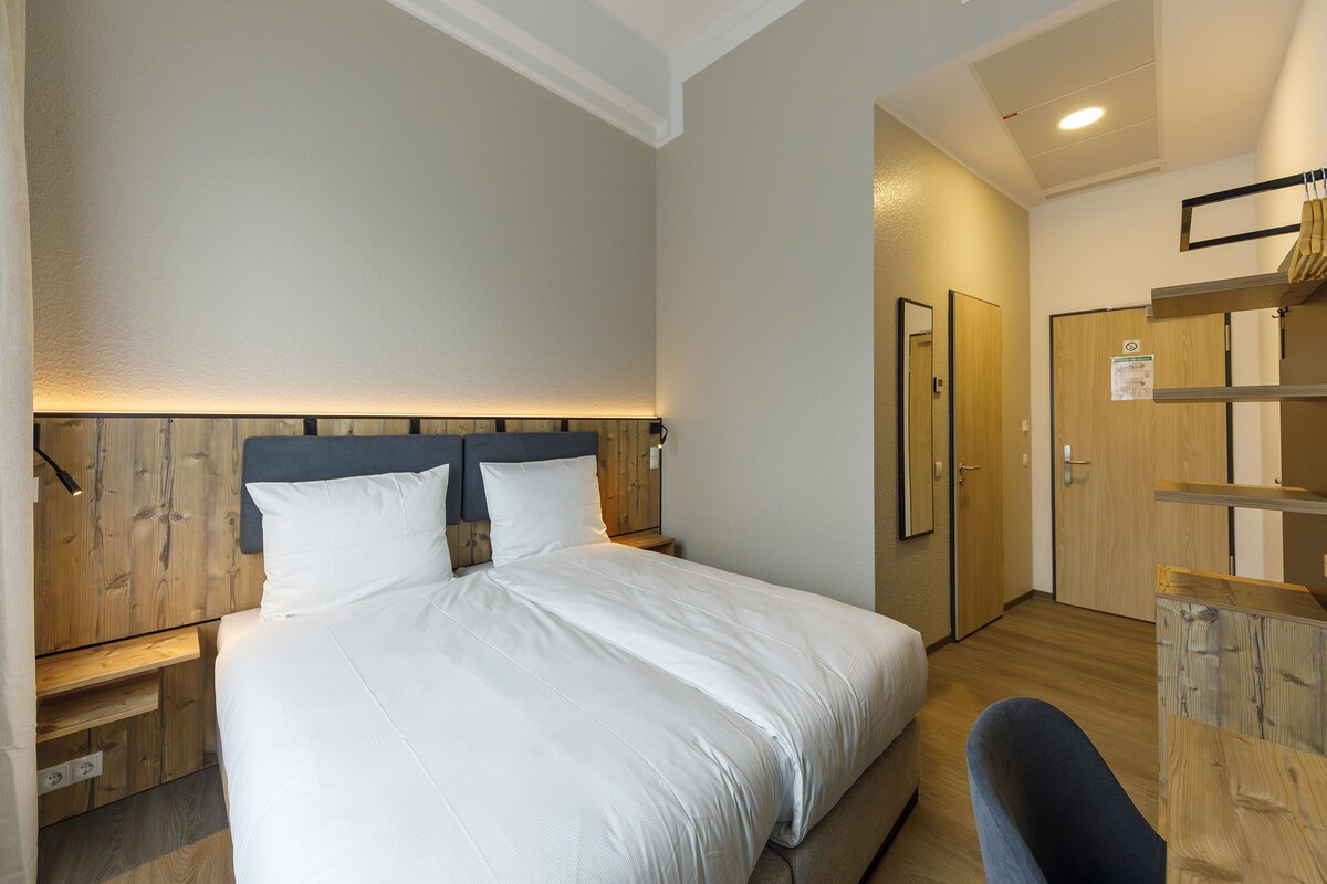A hotel room with a bed, bedside tables, a wardrobe, and a desk.