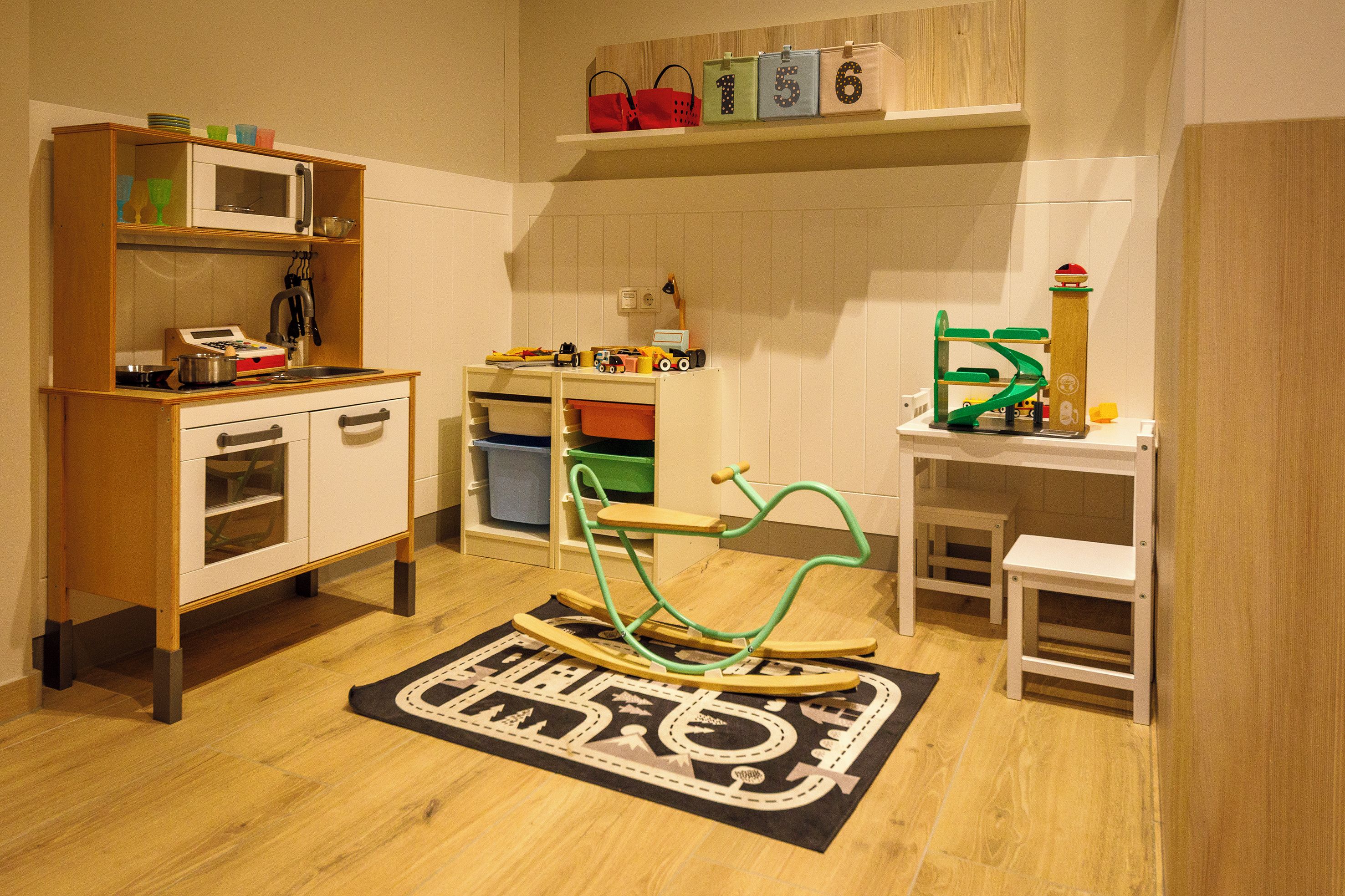 Un salón de juegos infantil con área de cocina, una mecedora y un tapete de juegos.