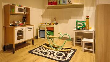 Un salón de juegos infantil con área de cocina, una mecedora y un tapete de juegos.