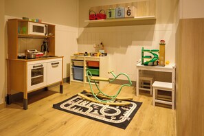 Un salón de juegos infantil con área de cocina, una mecedora y un tapete de juegos.