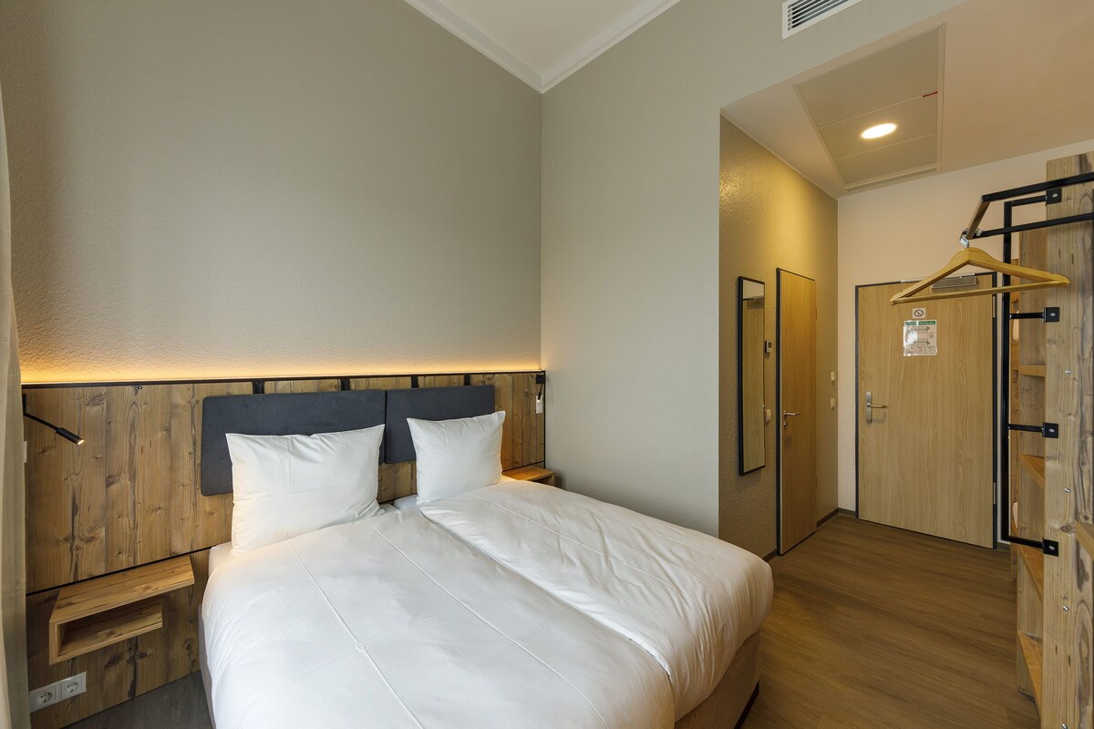 A hotel room with a bed, wooden headboard, bedside table, and a wardrobe with a mirror.