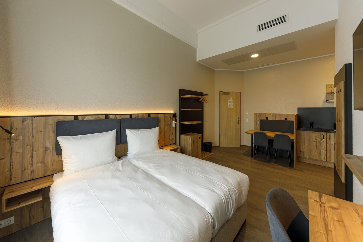 A hotel room with a large bed, a desk, and a chair.