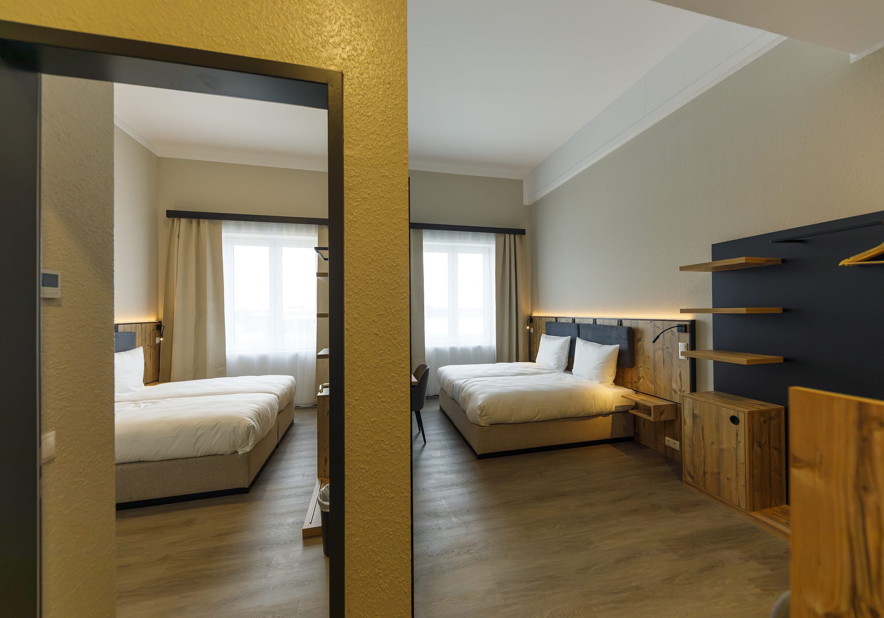 Ein Hotelzimmer mit zwei Betten, einem Holzkopfende, einem Schreibtisch und einem Spiegel.