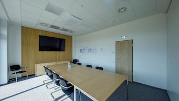Un salón de conferencias con una mesa larga, sillas, un televisor y una puerta con un letrero de salida de emergencia.