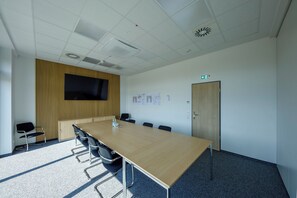 Un salón de conferencias con una mesa larga, sillas, un televisor y una puerta con un letrero de salida de emergencia.