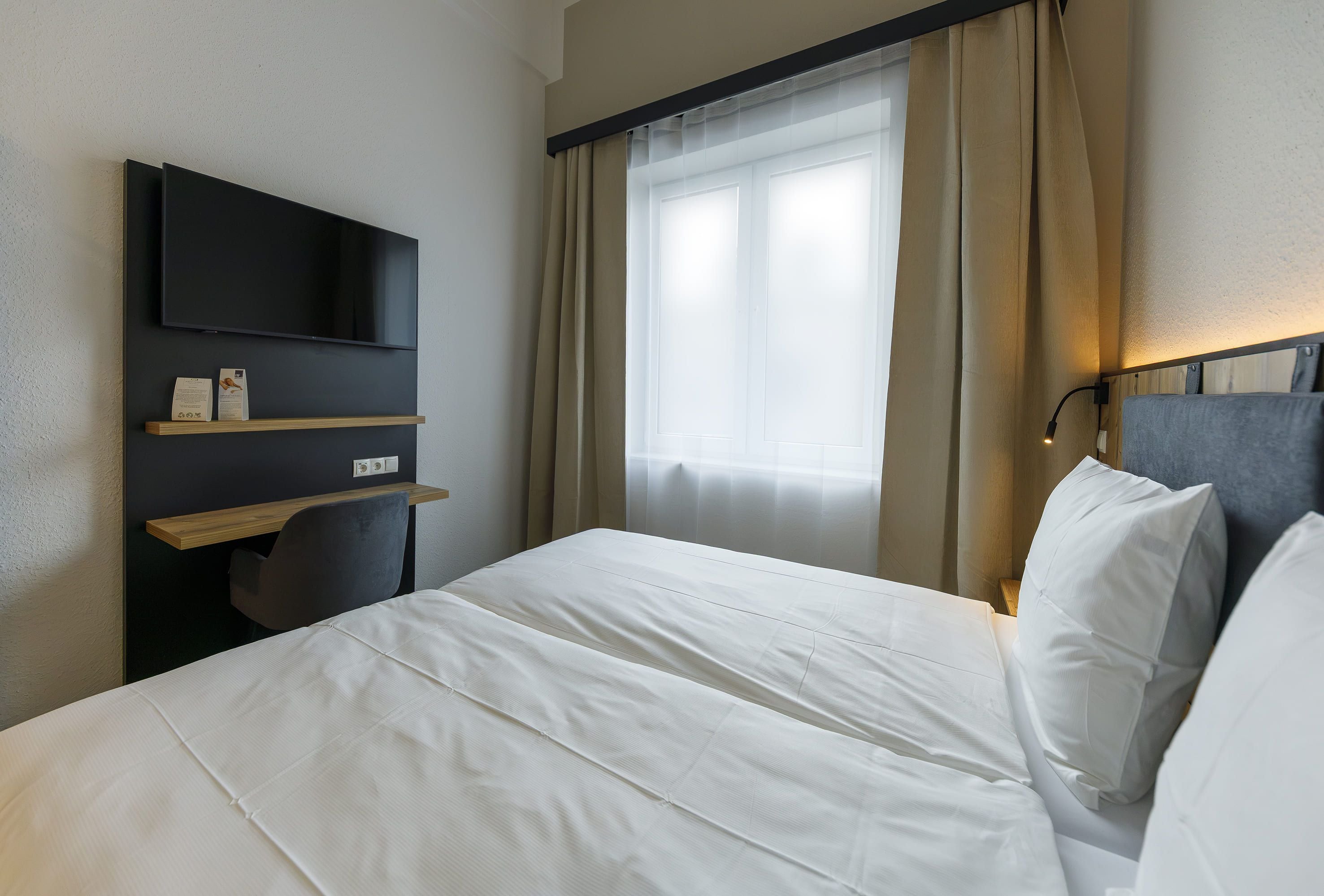 Una habitación de hotel con cama, escritorio, televisión de pantalla plana y ventana con cortinas.