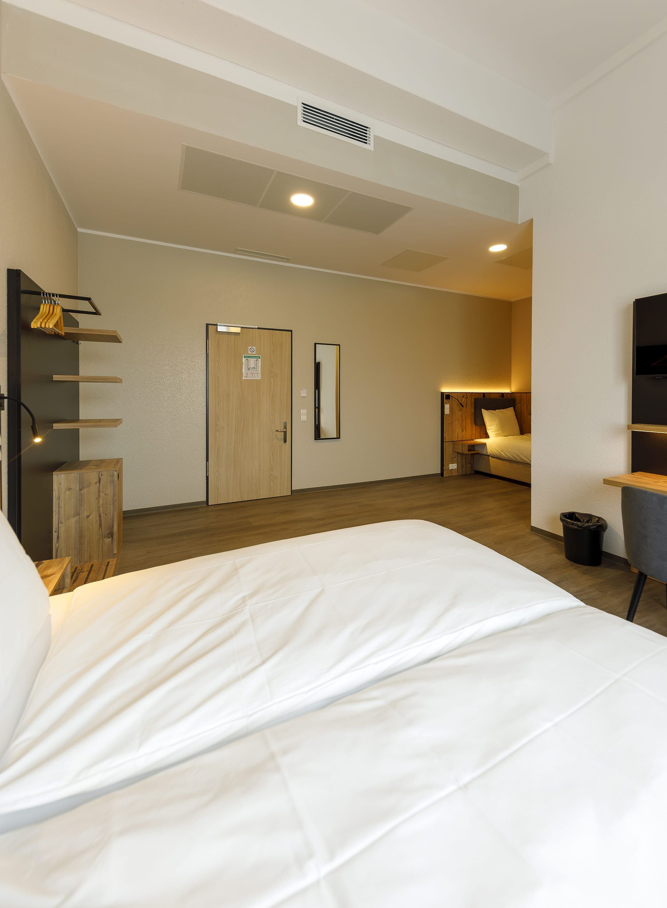 Habitación de hotel con cama, armario de madera, escritorio, silla, televisor y baño con ducha.