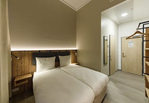 Habitación de hotel con una cama grande, cabecera de madera, mesitas de noche, un espejo y una puerta con un cartel.