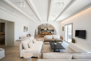 A spacious living area with a sofa set, a coffee table, and a television mounted on the wall. - Phos Chora - Six Bedroom Villa, Sleeps 12 (Mykonos)