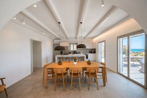 A modern kitchen with a central island, large windows, and a view of the sea. - Phos Chora - Six Bedroom Villa, Sleeps 12 (Mykonos)