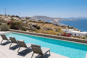 Ein Pool mit Liegestühlen, Meerblick und weiße Gebäude an einem Hang.