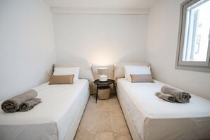 A small, clean room with two single beds, a bedside table with a lamp, and a window. - Phos Chora - Six Bedroom Villa, Sleeps 12 (Mykonos)