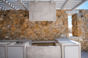 An outdoor kitchen area with stone walls and a metal roof structure. - Phos Chora - Six Bedroom Villa, Sleeps 12 (Mykonos)