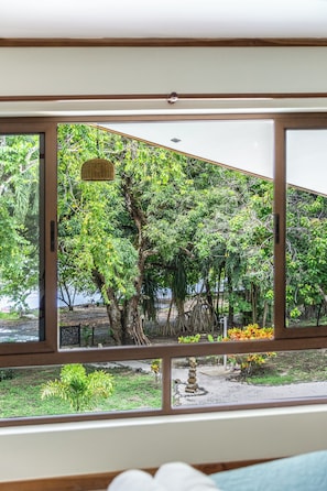 Ein Zimmer mit großem Fenster und Blick auf einen Garten mit Bäumen und einem kleinen Teich.