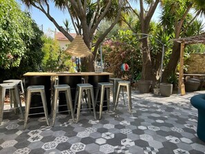 An outdoor bar area with a hexagonal tiled floor, metal stools, and a central bar counter. - Casa Moz House, Pool, Petanque (Marseille)