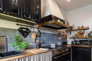 A modern kitchen with dark cabinetry, a central island, and a variety of cooking utensils and appliances. - Casa Moz House, Pool, Petanque (Marseille)