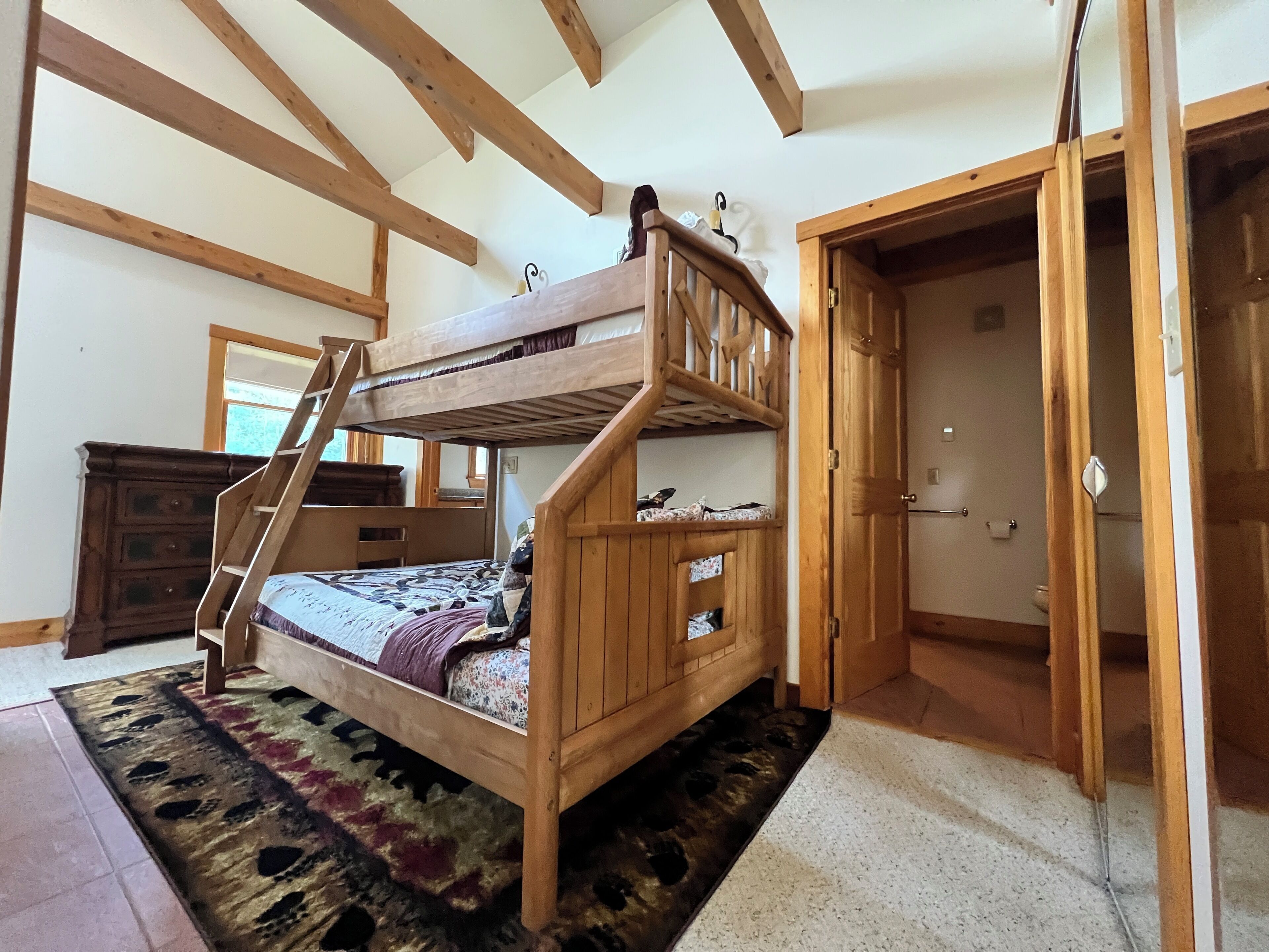 Un lit superposé avec une échelle, une commode en bois et une porte donnant sur une autre pièce.