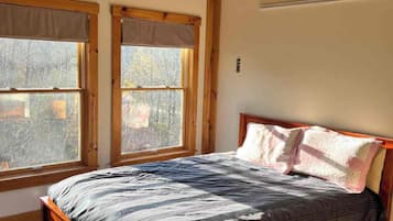 Un dormitorio con cama de madera, dos ventanas con persianas y una pared lisa.