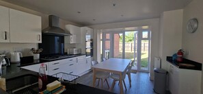 A modern kitchen with white cabinets, a stove, and a dining area with a table and chairs. - Sprawling 7-Bed Retreat in the Heart of Warboys (Warboys)