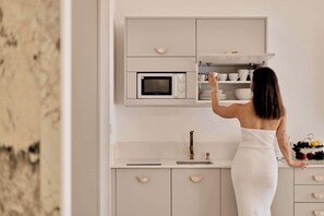 Eine Frau in einem weißen Kleid greift nach einer Tasse aus einem Schrank mit einer Mikrowelle darüber.