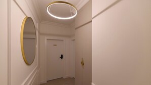 Een gang met een deur, een ronde spiegel en een moderne lamp.