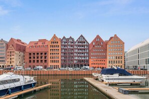 A marina with boats docked, a large red building with a modern design, and a clear sky. - Granaria B209A | Jacuzzi | Best Location (Gdańsk)