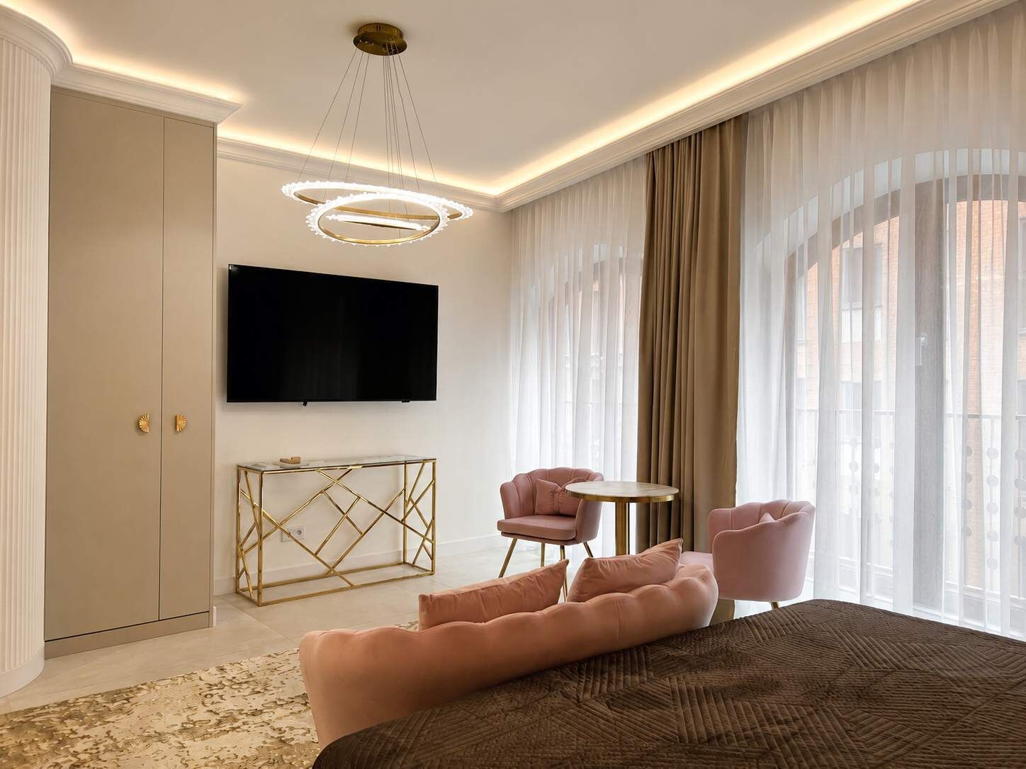 Una camera d'albergo moderna con un letto grande, una TV a parete, un piccolo tavolino rotondo e un angolo relax con due poltrone.