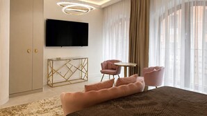 Ein modernes Hotelzimmer mit einem großen Bett, einem an der Wand befestigten Fernseher, einem kleinen runden Tisch und einer Sitzecke mit zwei Sesseln.