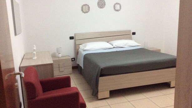 A bedroom with a bed, bedside tables, a chair, and a wall-mounted decoration. - Lorella's House (Terni)