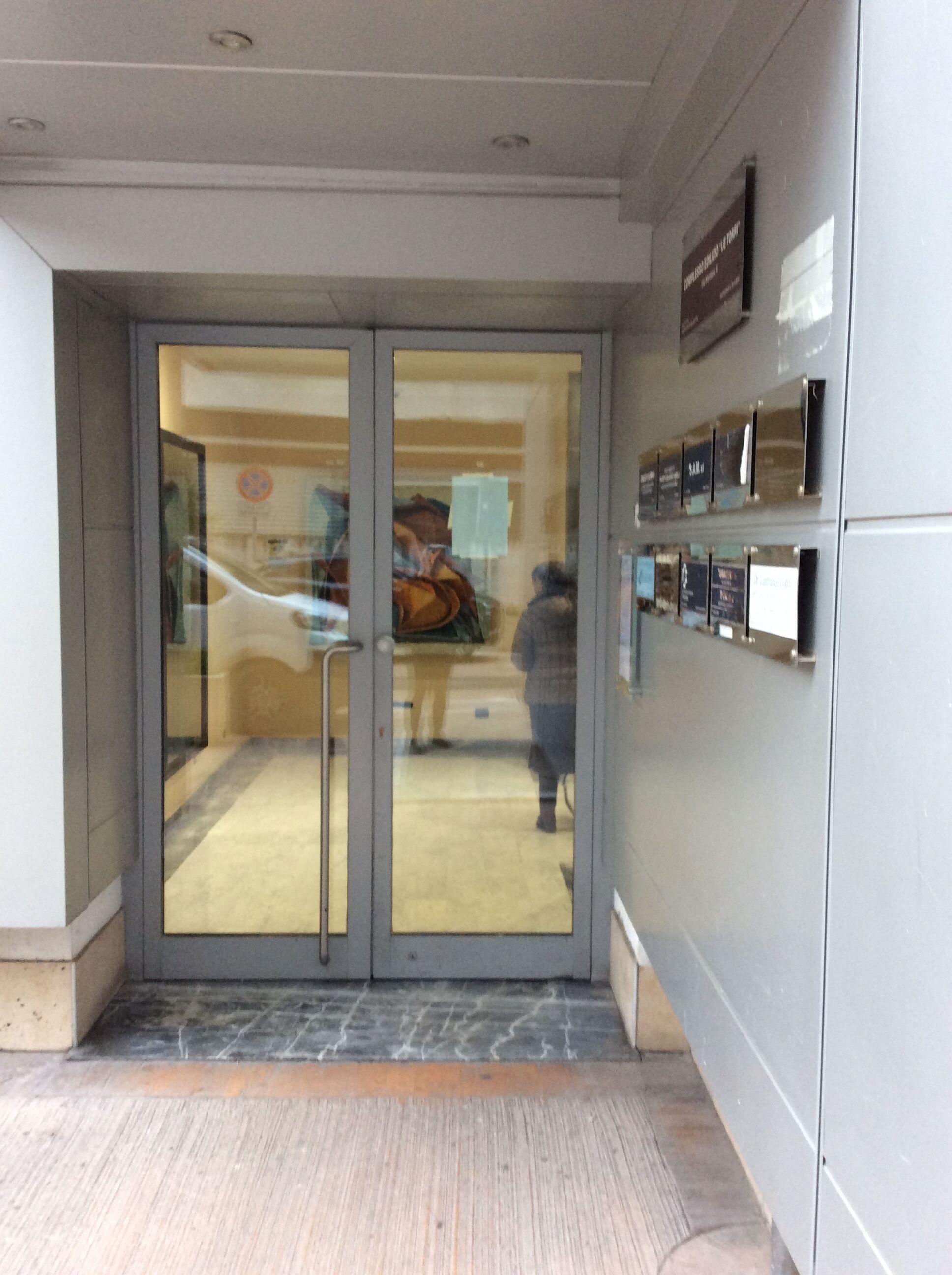 A hotel entrance with a glass door, a reception desk, and a wall-mounted directory.