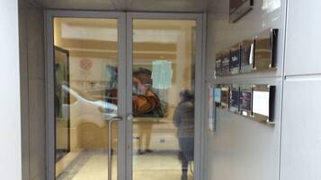 A hotel entrance with a glass door, a reception desk, and a wall-mounted directory.