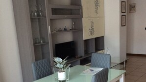 A dining area with a glass table, four chairs, a television, and a cabinet with decorative items. - Lorella's House (Terni)